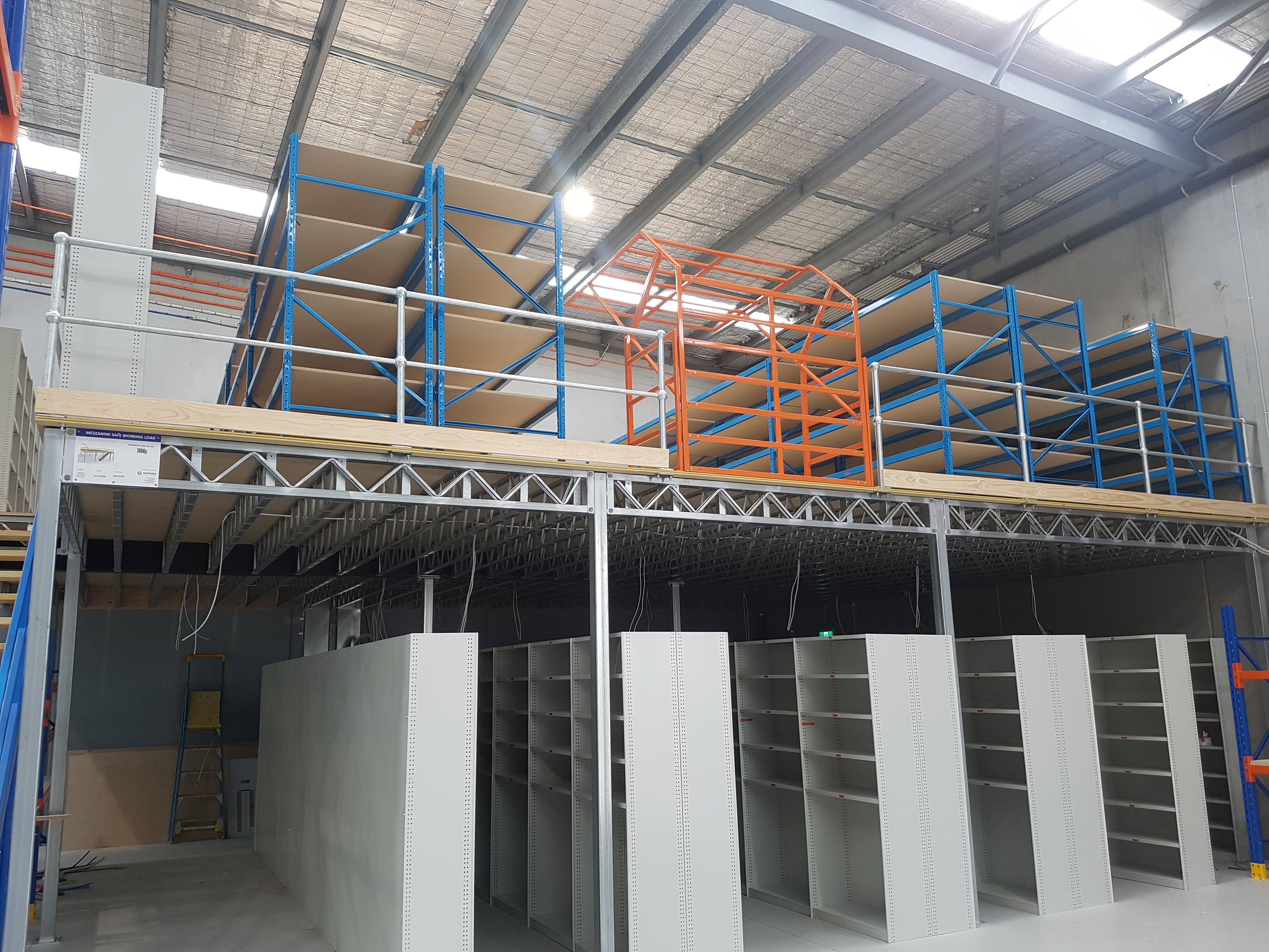 Clearspan mezzanine floor in a warehouse with an orange roll over gate and blue heavy duty longspan shelving 