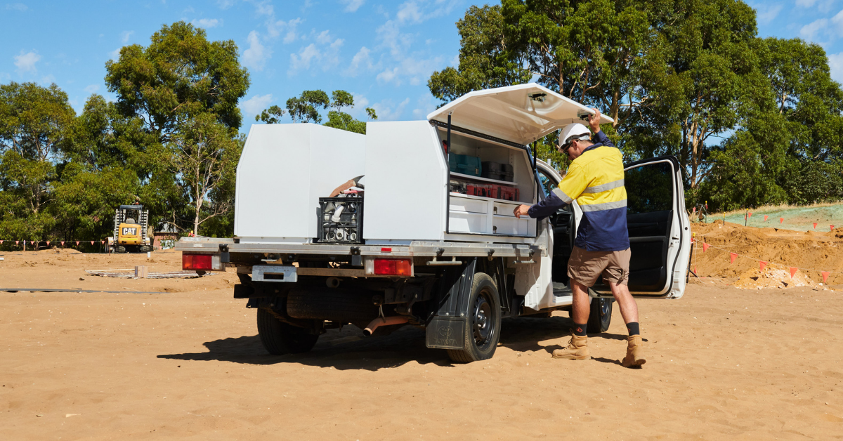 Tradesperson accessing an aluminium ute tool box and canopy storage system on a work vehicle at a construction site.