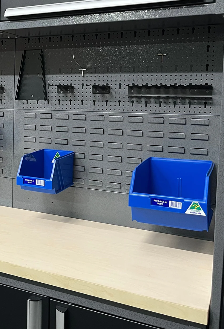 Two blue storage bins attached to a gray pegboard in a workshop setting.
